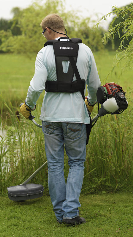 Brushcutter being used by model, garden location.