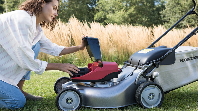 Side facing view of model demonstrating battery in lawnmower in garden location.