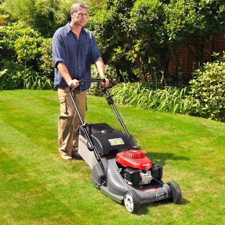 Front three-quarter, right facing lawnmower, being used by model, garden location.