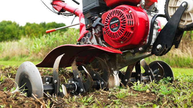 Close up of compact tiller, focusing on engine, garden location.