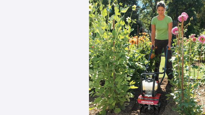 Honda tiller, front facing, being used by a model, garden location.