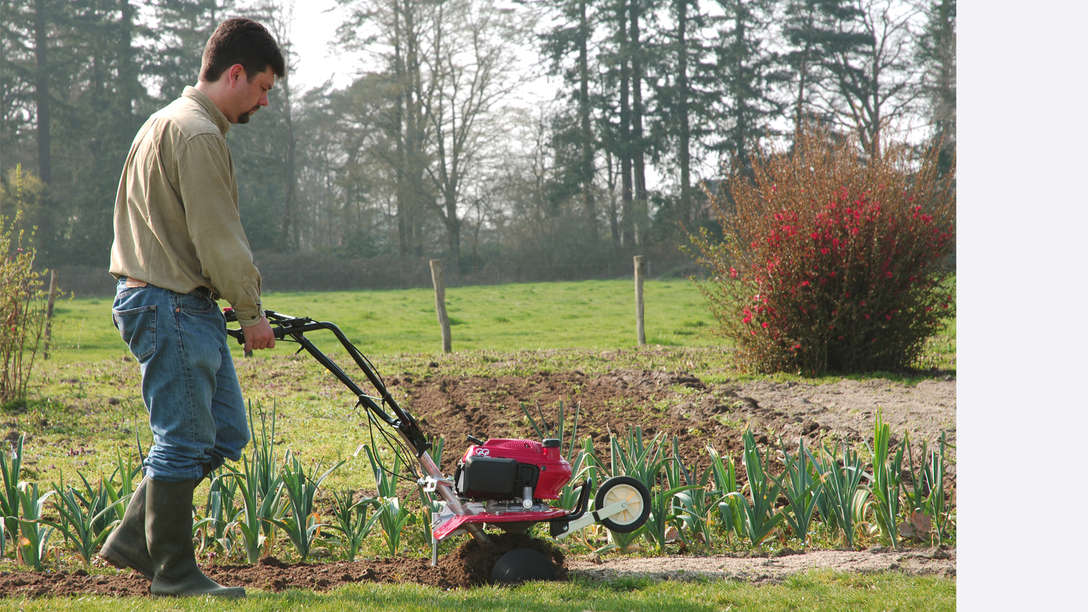 Mini tiller, right facing, being used by model, garden location.