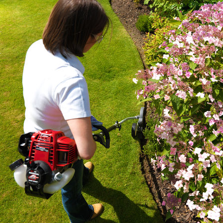 Honda Versatool, focusing on 4-stroke engine, being used by model, garden location.