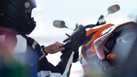 Rider adjusting his right glove sitting. Rear of motorcycle to rider's right.