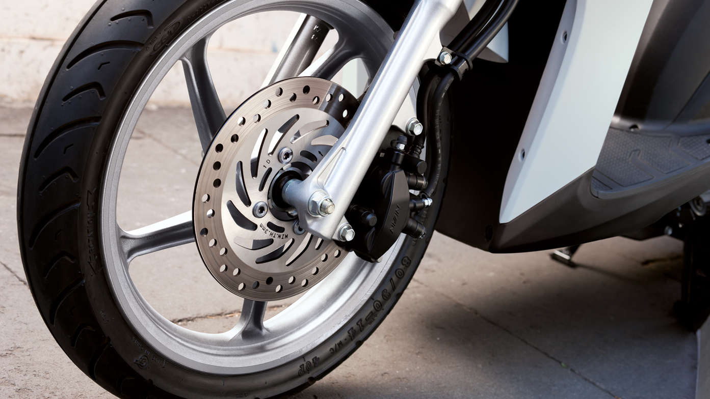 Honda Vision scooter front wheel focusing on CBS brakes. Left facing.